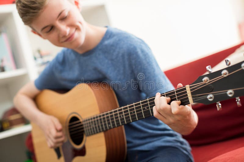 Adolescente che si siede su Sofa At Home Playing Guitar immagini stock Adolescente che si siede su Sofa At Home Playing Guitar immagini stock