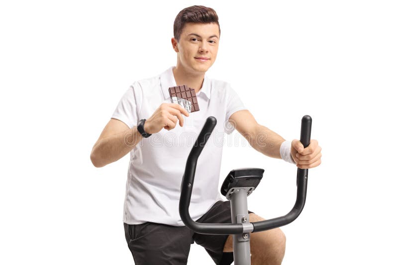 Adolescente com uma barra de chocolate que exercita em uma bicicleta estacionária fotografia de stock royalty free Adolescente com uma barra de chocolate que exercita em uma bicicleta estacionária fotografia de stock royalty free