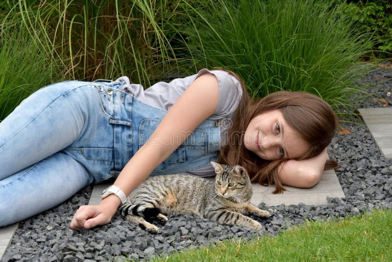 Teenage girl in the garden lying on the ground and cuddles with her young tabby cat. Teenage girl in the garden lying on the ground and cuddles with her young tabby cat