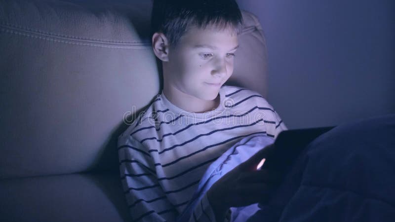 Adolescente con tablet pc en casa por la noche. niño pequeño jugando a juegos de ordenador ver video surf en la red almacen de video