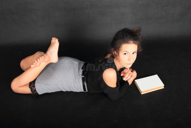 Concentrated teenage girl - smart schoolkid with brunette hair dressed in black blouse and grey skirt with an old book. School and education concept. Concentrated teenage girl - smart schoolkid with brunette hair dressed in black blouse and grey skirt with an old book. School and education concept.