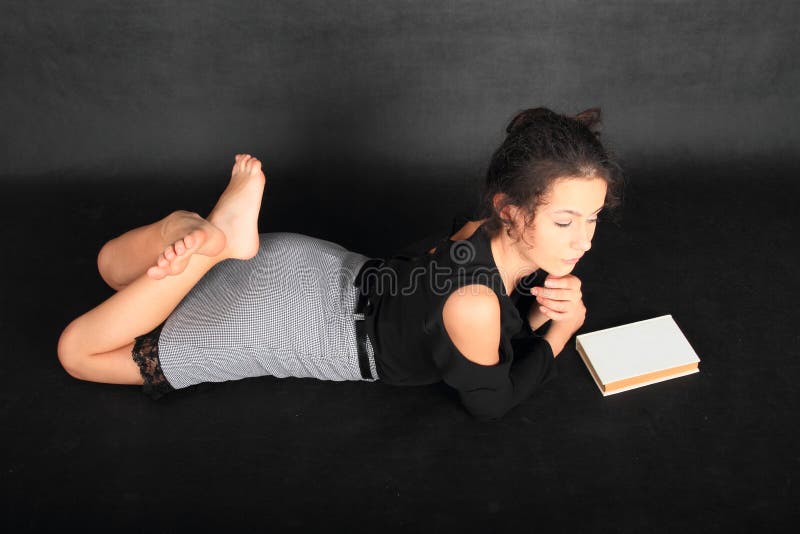 Concentrated teenage girl - smart schoolkid with brunette hair dressed in black blouse and grey skirt with an old book. School and education concept. Concentrated teenage girl - smart schoolkid with brunette hair dressed in black blouse and grey skirt with an old book. School and education concept.