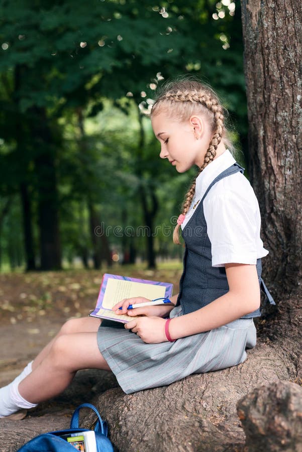 Adolescente da estudante que lê um livro em um parque perto de uma árvore foto de stock royalty free Adolescente da estudante que lê um livro em um parque perto de uma árvore foto de stock royalty free