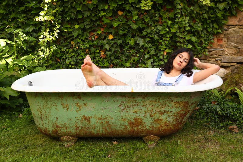 Teenage girl - barefoot schoolkid lying in an old bathtub with bare feet out. Outdoor with wall overgrown with ivy behind. Retro home related portrait concept. Teenage girl - barefoot schoolkid lying in an old bathtub with bare feet out. Outdoor with wall overgrown with ivy behind. Retro home related portrait concept.