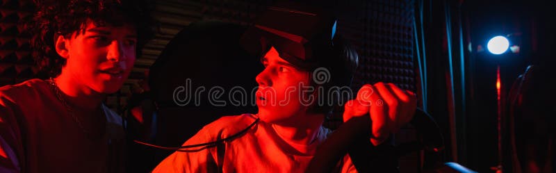 Adolescente entusiasta sul simulatore di un'auto vicino. Adolescente entusiasta sul simulatore di auto vicino a un amico in vr play zone banner immagine stock