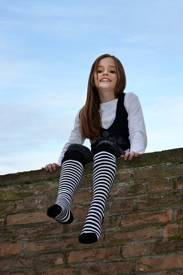 Teenage girl with black and white striped socks sitting on a wall in the garden. Teenage girl with black and white striped socks sitting on a wall in the garden