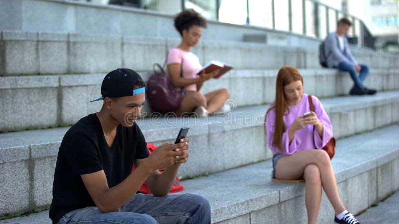 Adolescente negro chateando el smartphone al aire libre, estudiantes de secundaria en pausa fotos de archivo libres de regalías