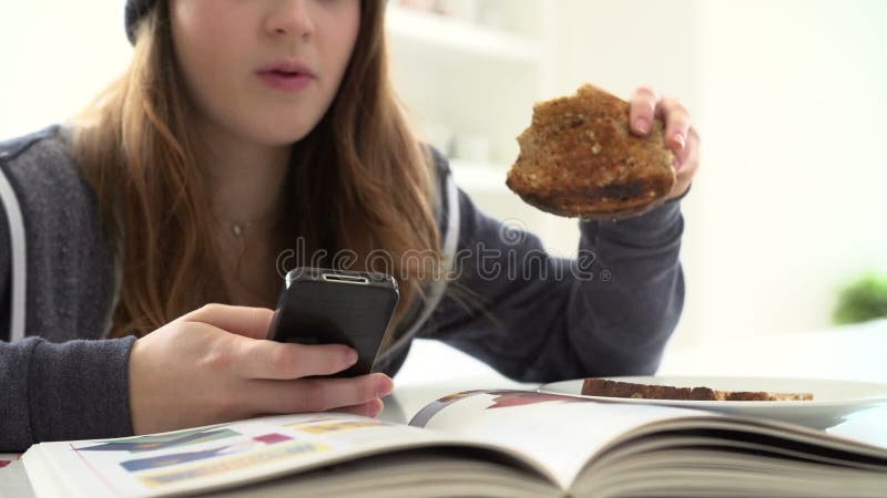 Adolescente que come o café da manhã enquanto enviando a mensagem de texto