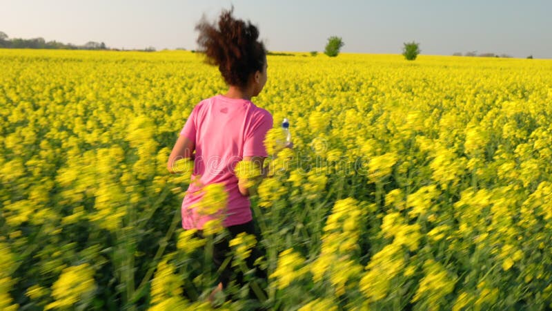 Adolescente que corre com uma garrafa de água no campo de flores amarelas