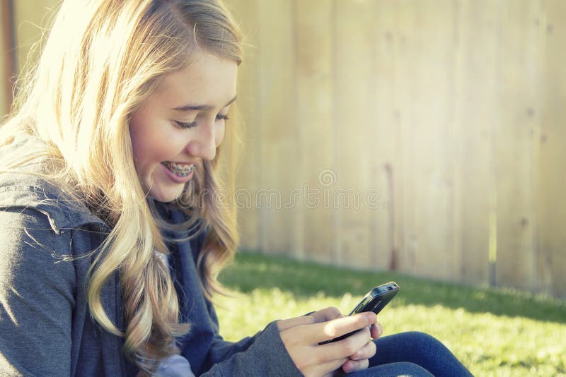 Adolescente que sorri ao usar um telefone celular imagens de stock Adolescente que sorri ao usar um telefone celular imagens de stock