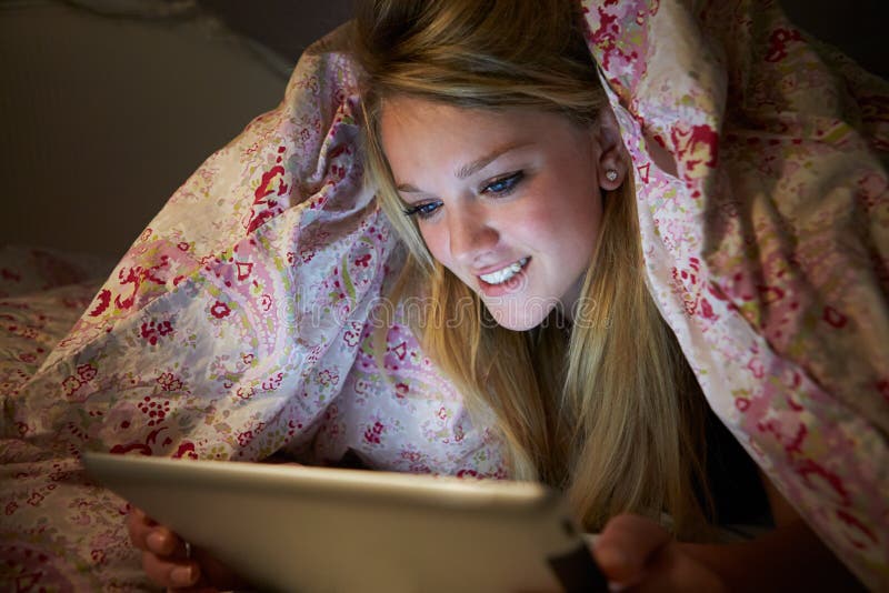 Adolescente que usa la tableta de Digitaces en cama en la noche imágenes de archivo libres de regalías Adolescente que usa la tableta de Digitaces en cama en la noche imágenes de archivo libres de regalías