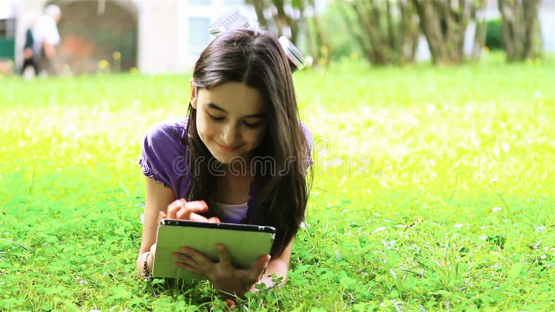 Adolescente que usa a tabuleta digital na grama