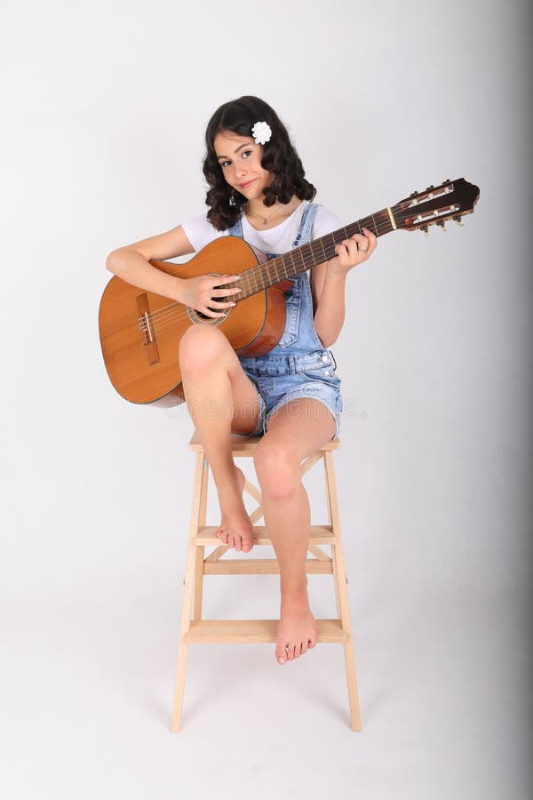 Smiling teenage girl - schoolkid with brunette hair dressed in white t-shirt and blue jeans shorts playing classic guitar. Music and musical instrument concept. Smiling teenage girl - schoolkid with brunette hair dressed in white t-shirt and blue jeans shorts playing classic guitar. Music and musical instrument concept.