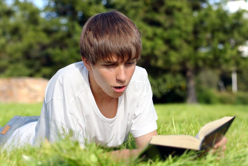 Surprised Teenager lying on the Grass and reads a Book in the Summer Park. Surprised Teenager lying on the Grass and reads a Book in the Summer Park