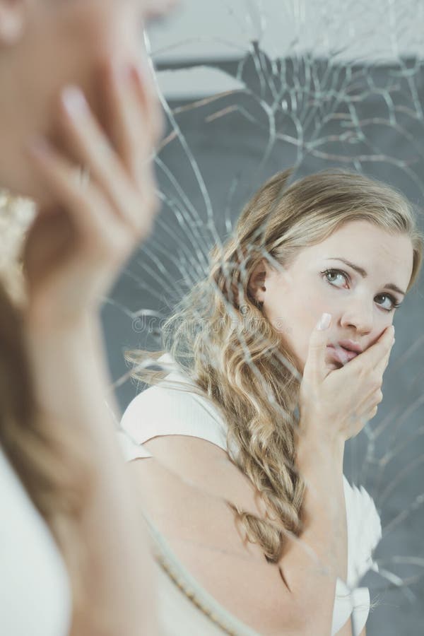 Beautiful depressed teenage girl with personality disorders looking in the broken mirror. Beautiful depressed teenage girl with personality disorders looking in the broken mirror