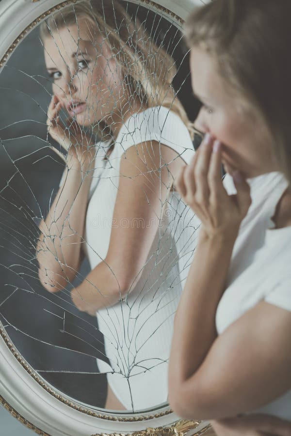 Pretty scared teenager with personality disorders looking in the broken mirror. Pretty scared teenager with personality disorders looking in the broken mirror