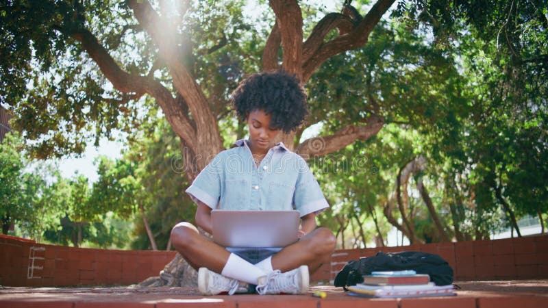 Adolescente étudiante ordinateur portable assis parc ensoleillé. jeune africain décontracté. banque de vidéos