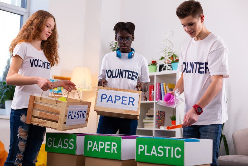 Adolescentes activos que separan el papel del plástico mientras que clasifica la basura foto de archivo Adolescentes activos que separan el papel del plástico mientras que clasifica la basura foto de archivo