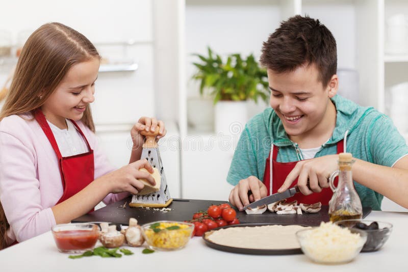 Adolescentes felizes que têm o divertimento na cozinha que prepara uma pizza fotografia de stock Adolescentes felizes que têm o divertimento na cozinha que prepara uma pizza fotografia de stock
