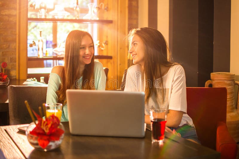 Teenage girls talking and having fun together while sitting near laptop in cafe bar. Teenage girls talking and having fun together while sitting near laptop in cafe bar