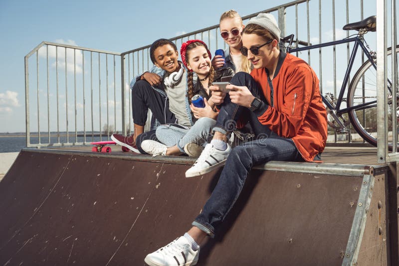 Adolescentes que se divierten con smartphone en parque del monopatín imagen de archivo Adolescentes que se divierten con smartphone en parque del monopatín imagen de archivo