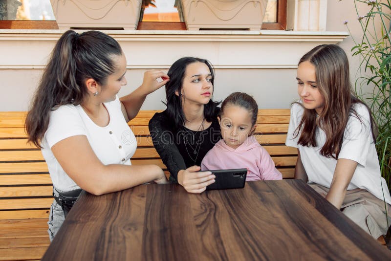 teenagers and one child having fun outdoors in a cafe. Friendship of children and teenagers. Four girls, dressed in different clothes, shout on the phone. teenagers and one child having fun outdoors in a cafe. Friendship of children and teenagers. Four girls, dressed in different clothes, shout on the phone