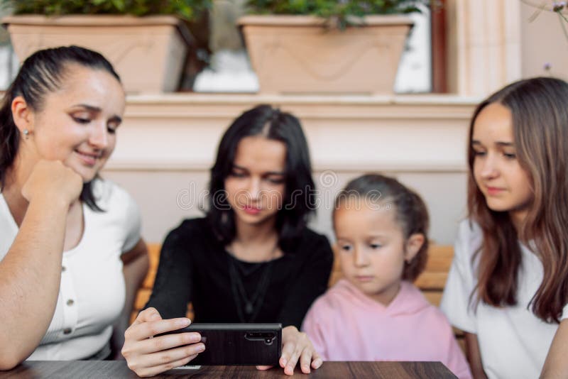 teenagers and one child having fun outdoors in a cafe. Friendship of children and teenagers. Four girls, dressed in different clothes, shout on the phone. teenagers and one child having fun outdoors in a cafe. Friendship of children and teenagers. Four girls, dressed in different clothes, shout on the phone