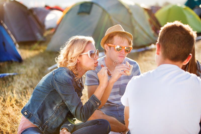 Adolescents s'asseyant au sol devant des tentes, mangeant photographie stock libre de droits Adolescents s'asseyant au sol devant des tentes, mangeant photographie stock libre de droits