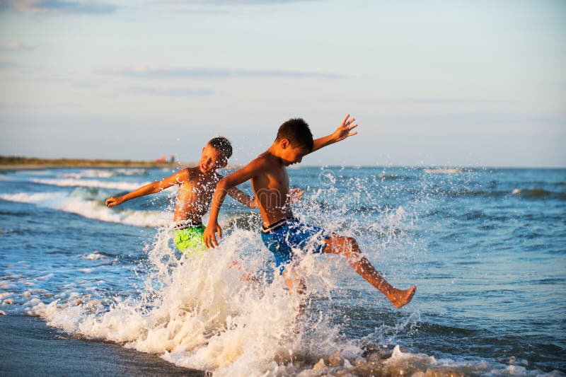 Adolescência de dois meninos que joga na água do mar que espirra o wat dos pés fotografia de stock Adolescência de dois meninos que joga na água do mar que espirra o wat dos pés fotografia de stock