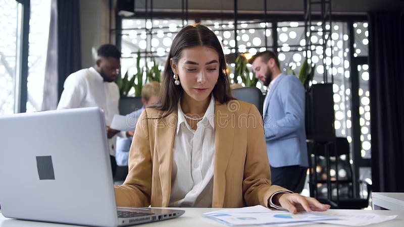 Adorabele jonge, doelgerichte zakenvrouw die blij is met succesvolle resultaten op het computerscherm in het moderne kantoor op d