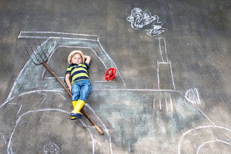 Adorabil băiețel jucându-se cu cretă colorată și pictând o imagine mare de tractor pe asfalt. Copil preșcolar fericit joc stock images