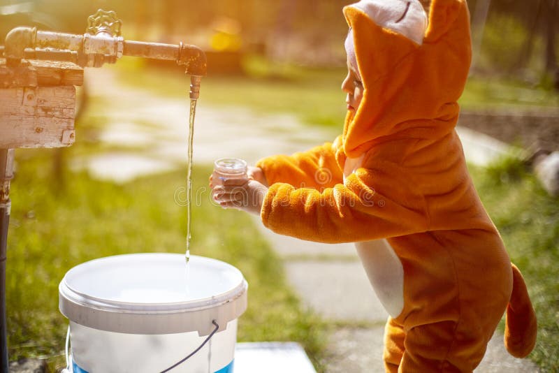 Adorabile bimbo gioca con l'acqua e il rubinetto al sole fotografia stock