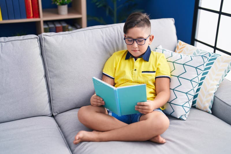 Adorabile ragazzo ispanico che legge un libro sul divano di casa immagine stock libera da diritti