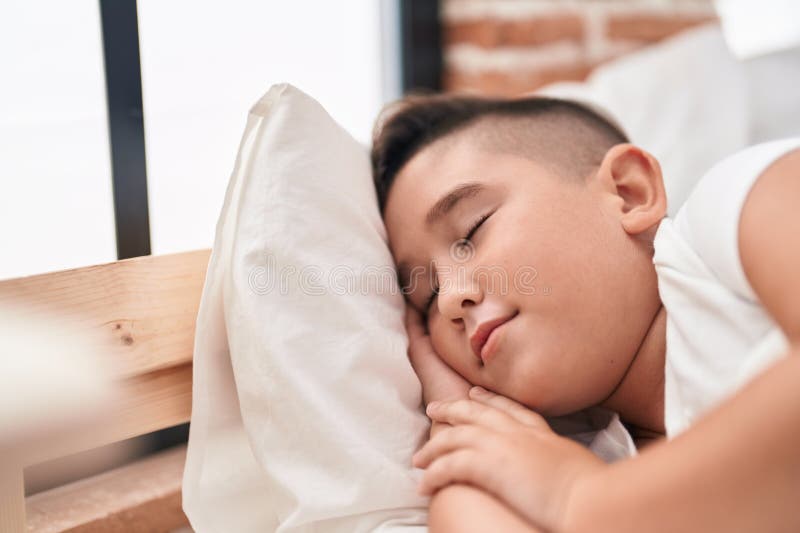Adorabile ragazzo ispanico sdraiato sul letto a dormire in camera da letto fotografia stock
