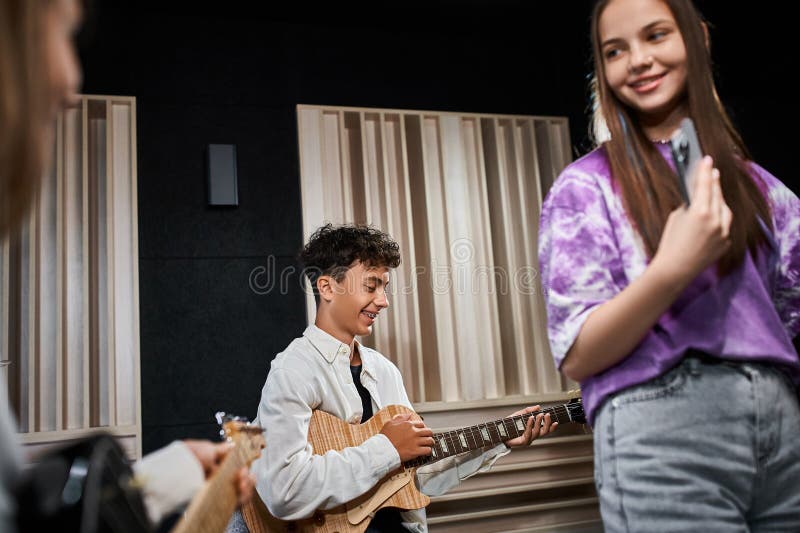 adorable teenage boy with braces in casual outfit playing guitar next to his friends, musical group, stock photo. adorable teenage boy with braces in casual outfit playing guitar next to his friends, musical group, stock photo