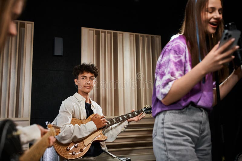 adorable cute teenager playing guitar and looking attentively at his friends, musical group, stock photo. adorable cute teenager playing guitar and looking attentively at his friends, musical group, stock photo