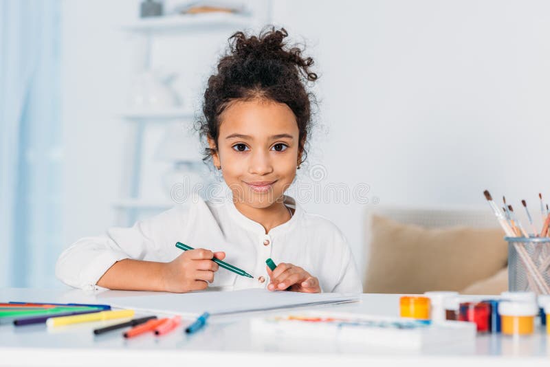 adorable african american kid drawing with felt pens and looking at camera