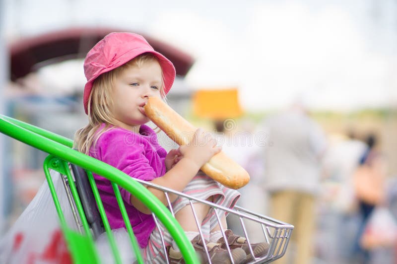 Adorable baby eat long bread, sit in cart