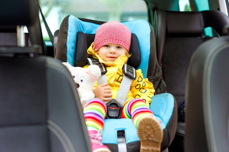 Adorable baby girl with blue eyes and in colorful clothes sitting in car seat. Toddler child in winter clothes going on.