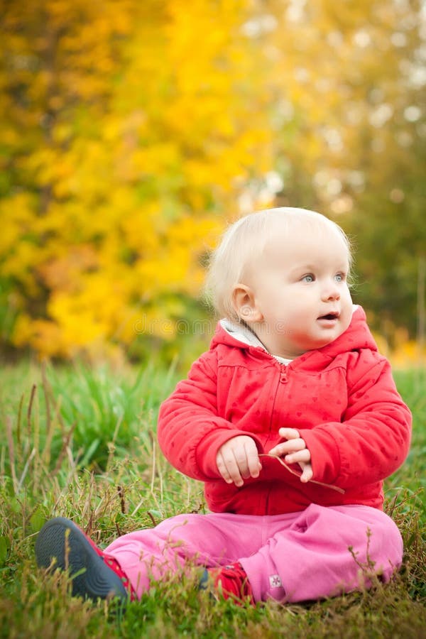 Adorable baby sit on grass under yellow tree