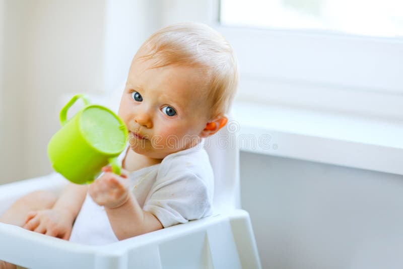 Adorable baby sitting in chair and holding cup