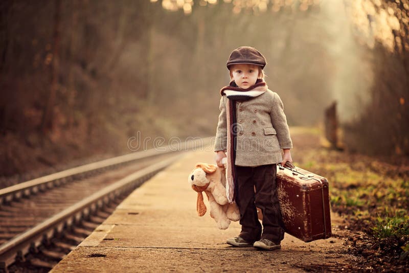 Adorabile ragazzo in una stazione ferroviaria, in attesa del treno con la valigia e orsetto.