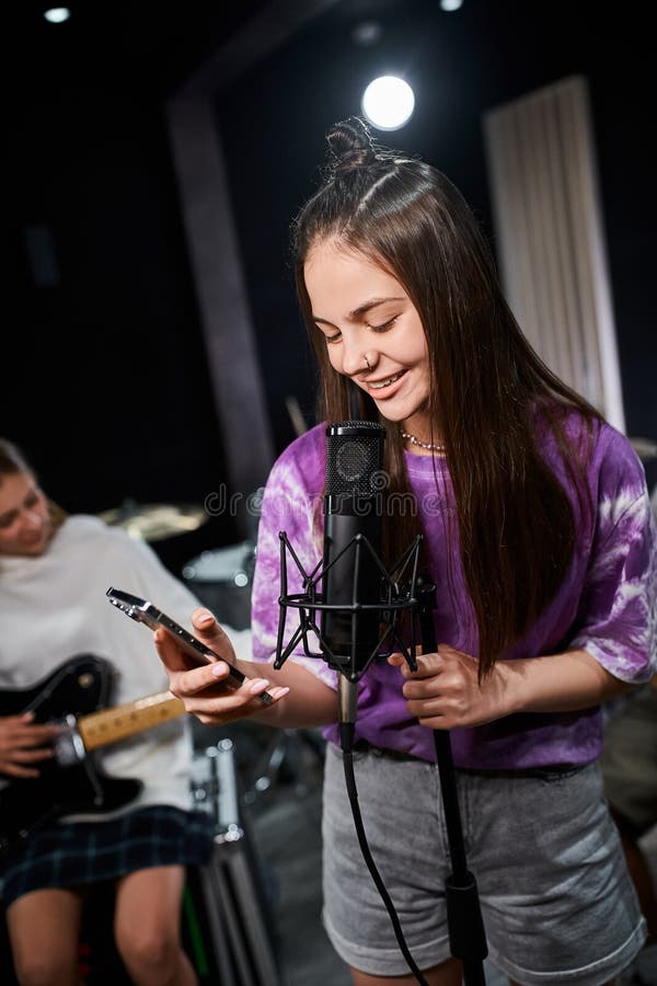 adorable pretty teenage girl in vibrant attire looking at phone and singing next to her friends, stock photo. adorable pretty teenage girl in vibrant attire looking at phone and singing next to her friends, stock photo