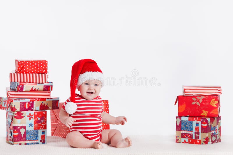 Adorable child in santa cap with stacks of present boxes around sitting on the floor. Isolated on white background