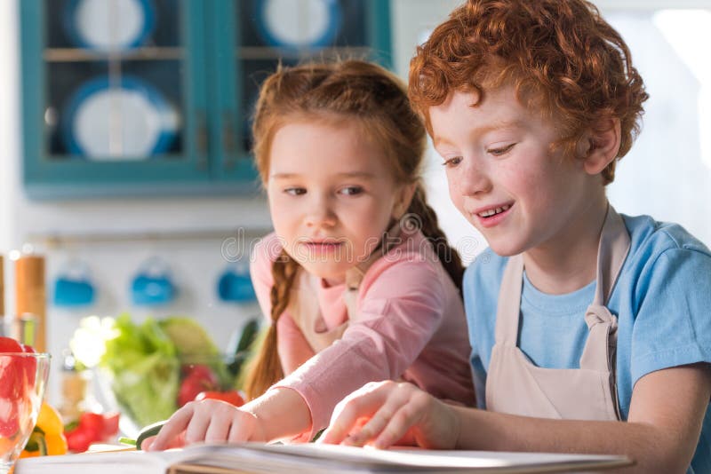 Adorable Children Reading Cookbook while Cooking Together Stock Photo