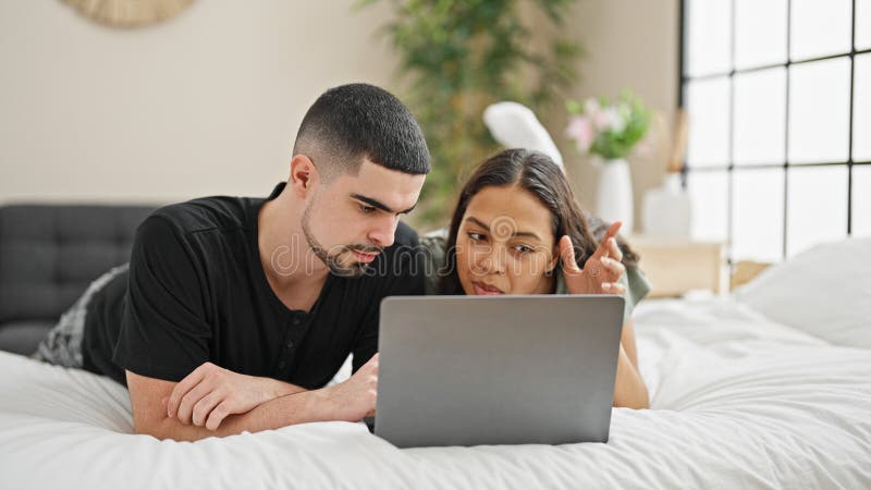 Adorable couple smiling and relaxing at home, lying in bed chatting and enjoying a lovely video call in their cosy, beautifully designed bedroom