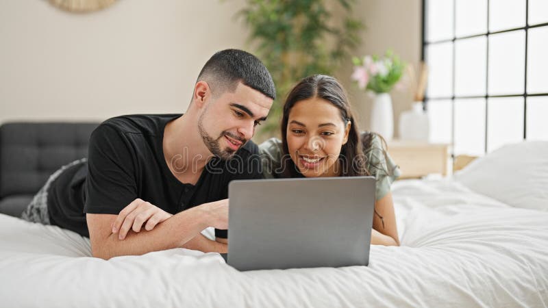 Adorable couple smiling and relaxing at home, lying in bed chatting and enjoying a lovely video call in their cosy, beautifully. Designed bedroom