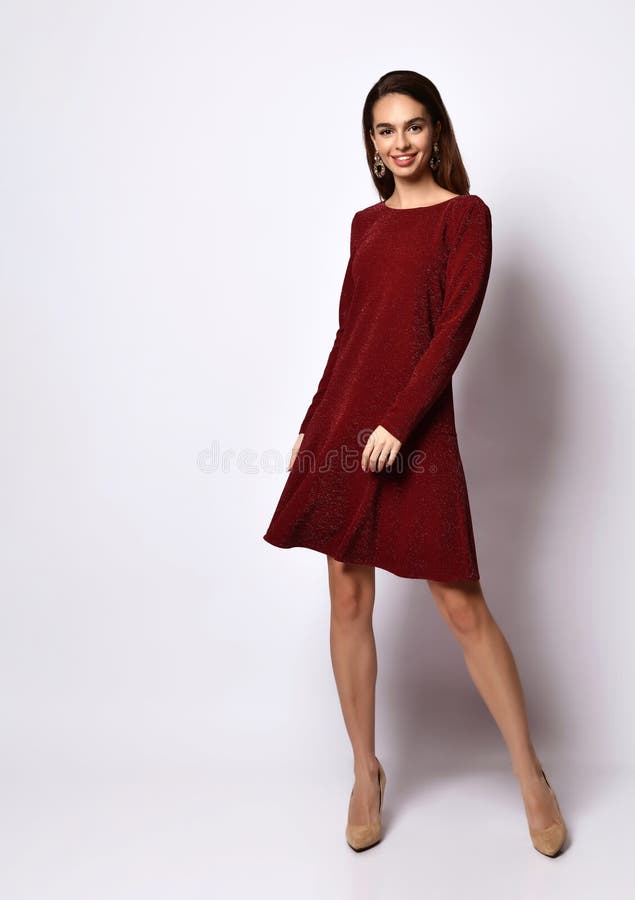 Gorgeous dark-haired young woman standing hands on hips in elegant dark-red sequin dress with long sleeves and nude stilettos. Adorable dark-haired young woman royalty free stock image Gorgeous dark-haired young woman standing hands on hips in elegant dark-red sequin dress with long sleeves and nude stilettos. Adorable dark-haired young woman royalty free stock image