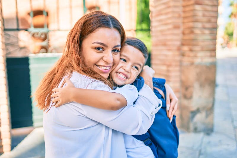 Adorable estudiante latino y mamá abrazándose en la ciudad imagen de archivo libre de regalías