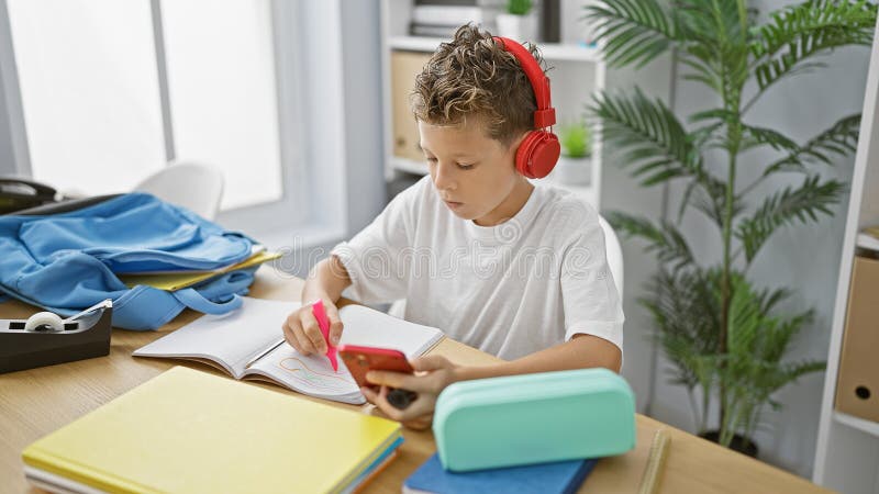 Adorable estudiante rubio envuelto en escuchar música en su smartphone dibujando diligentemente en un aula imágenes de archivo libres de regalías
